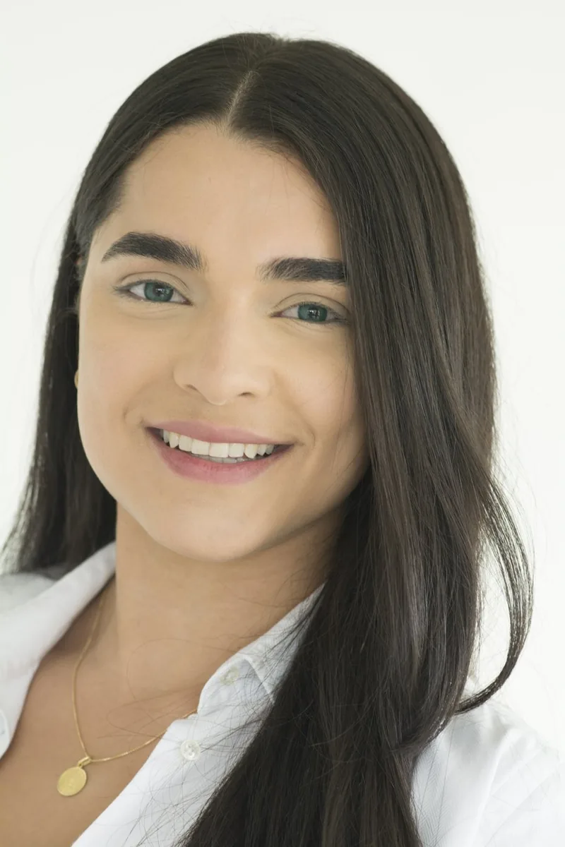 Mujer de cabello oscuro y largo sonriendo, con camisa blanca